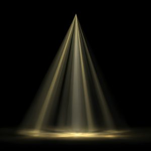 A single spotlight shining onto an empty stage in darkness, symbolising the pressure and visibility placed on people who appear on reality television.