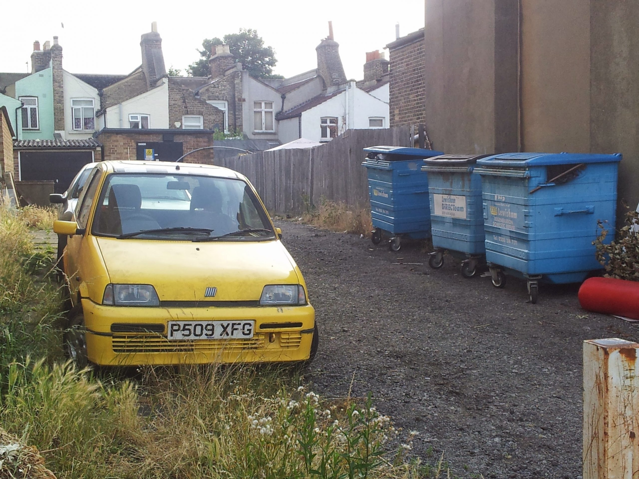 Yellow car parked beside blue commercial bins behind a row of South London houses